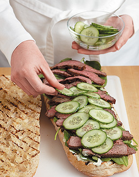Spread the green goddess over the bottom half of the bread, then layer with spinach, steak, and cucumbers.