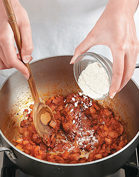 Stir tomato paste and flour into the saut&eacute;ed onions. They will help thicken the liquids into a rich sauce.