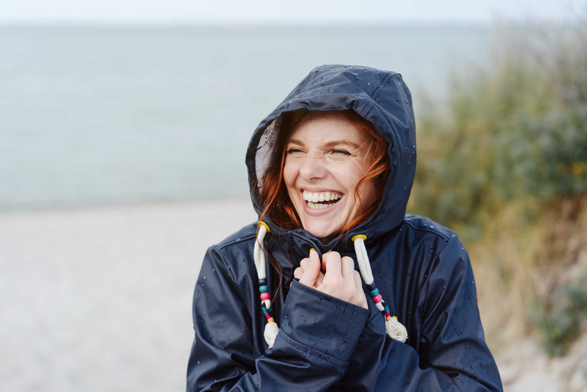 Glad kvinna i jacka på stranden