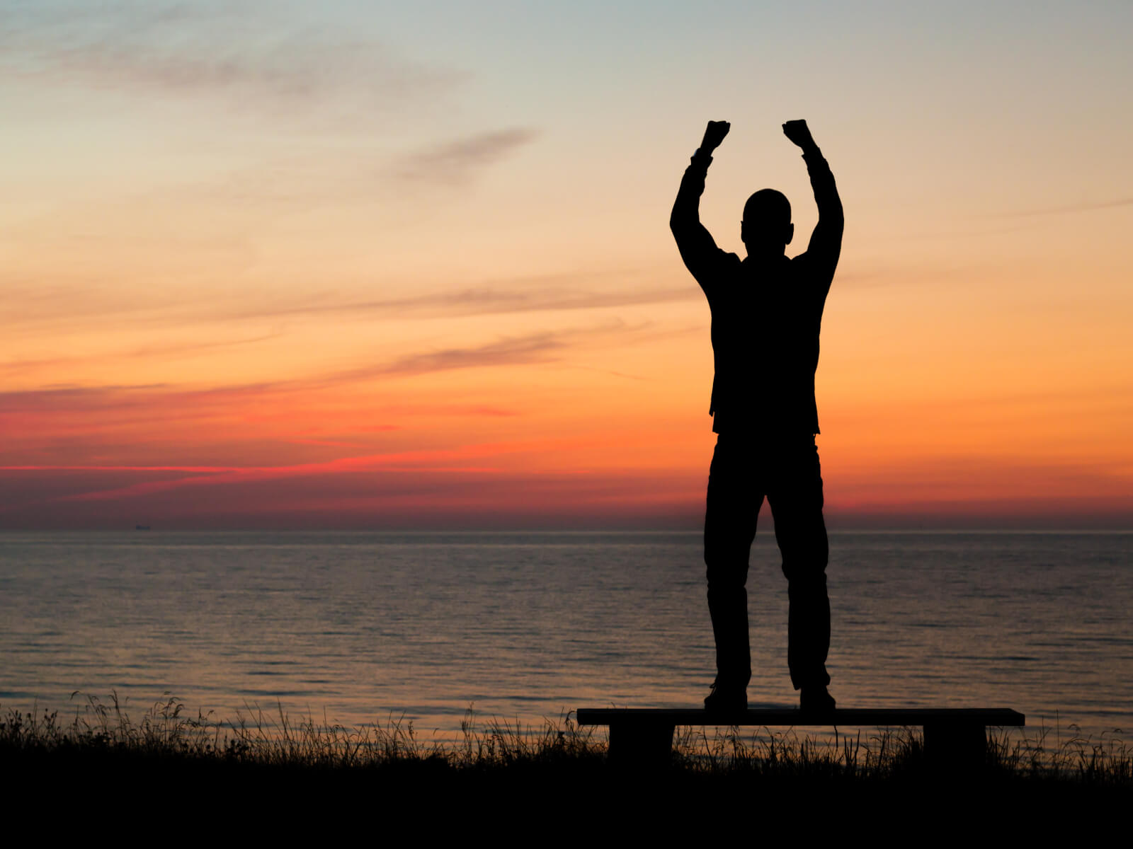Man sträcker upp armarna mot himlen i solnedgången