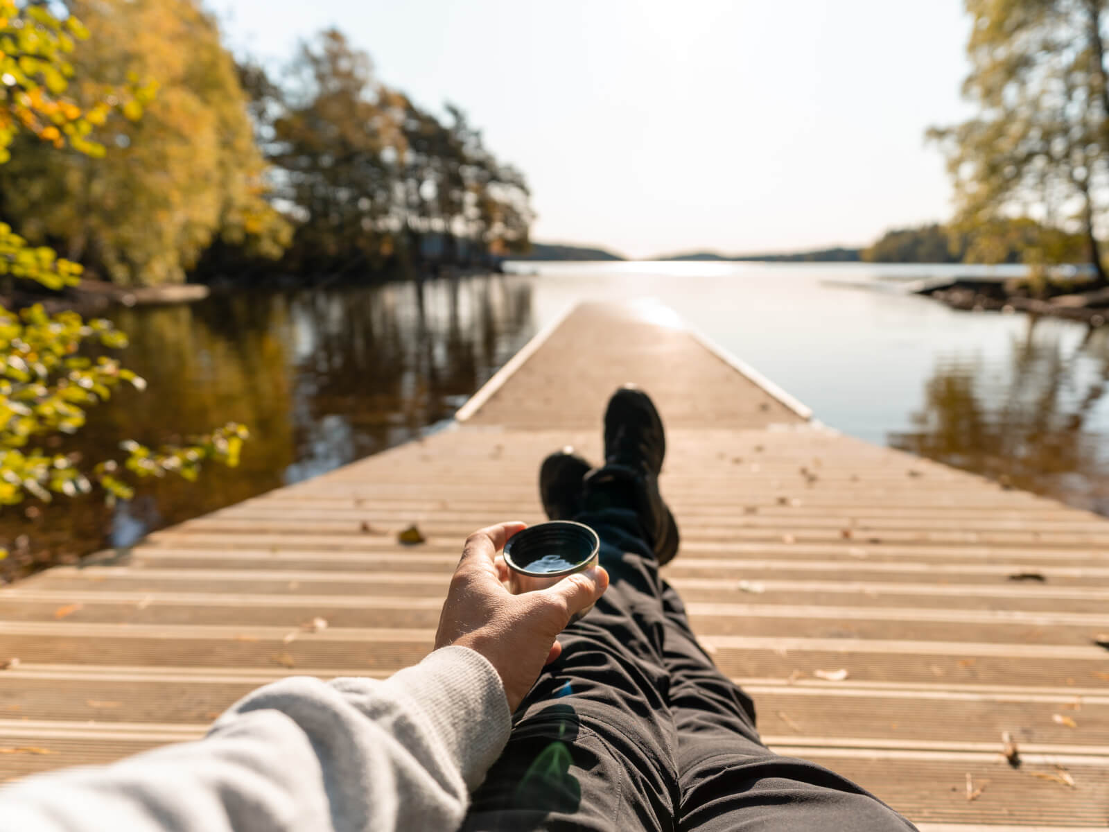 Man njuter på en brygga med en kaffekopp i handen.