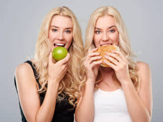Kvinnliga tvillingar äter äpple och hamburgare