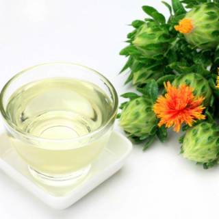 a bowl containing a clear oil, next to an orange safflower leaf