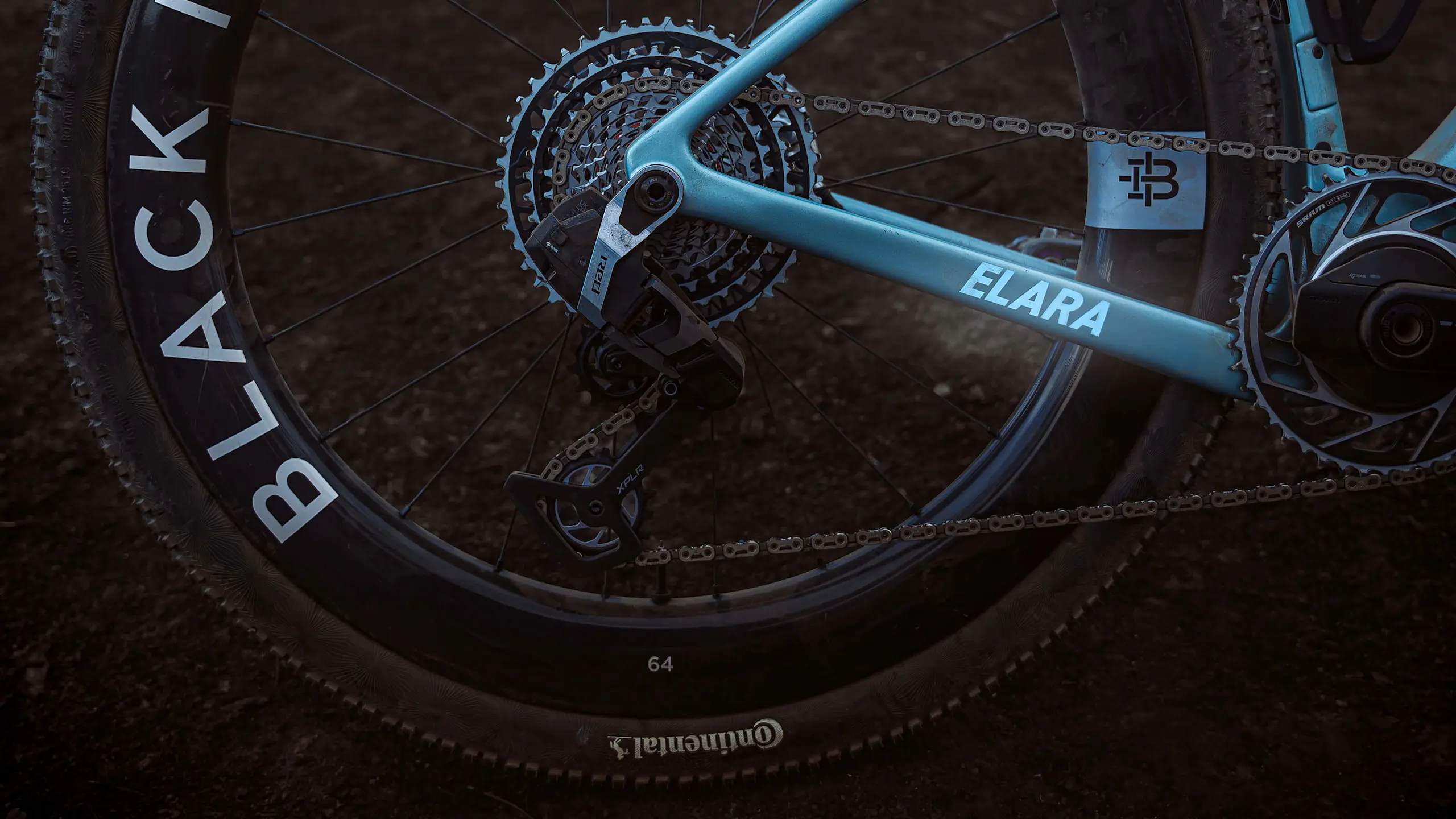 Close-up drivetrain side view of the ELARA rear derailleur and Black Ince 64 wheels. Dark lighting helps the bike colour pop.