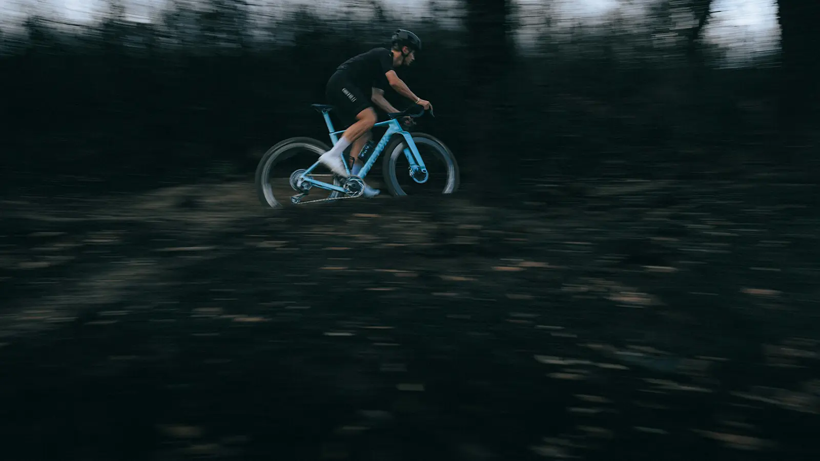 Split shot with a riding image at the top and a drivetrain side view of the ELARA in Virescent Blue below. Dark lighting. 