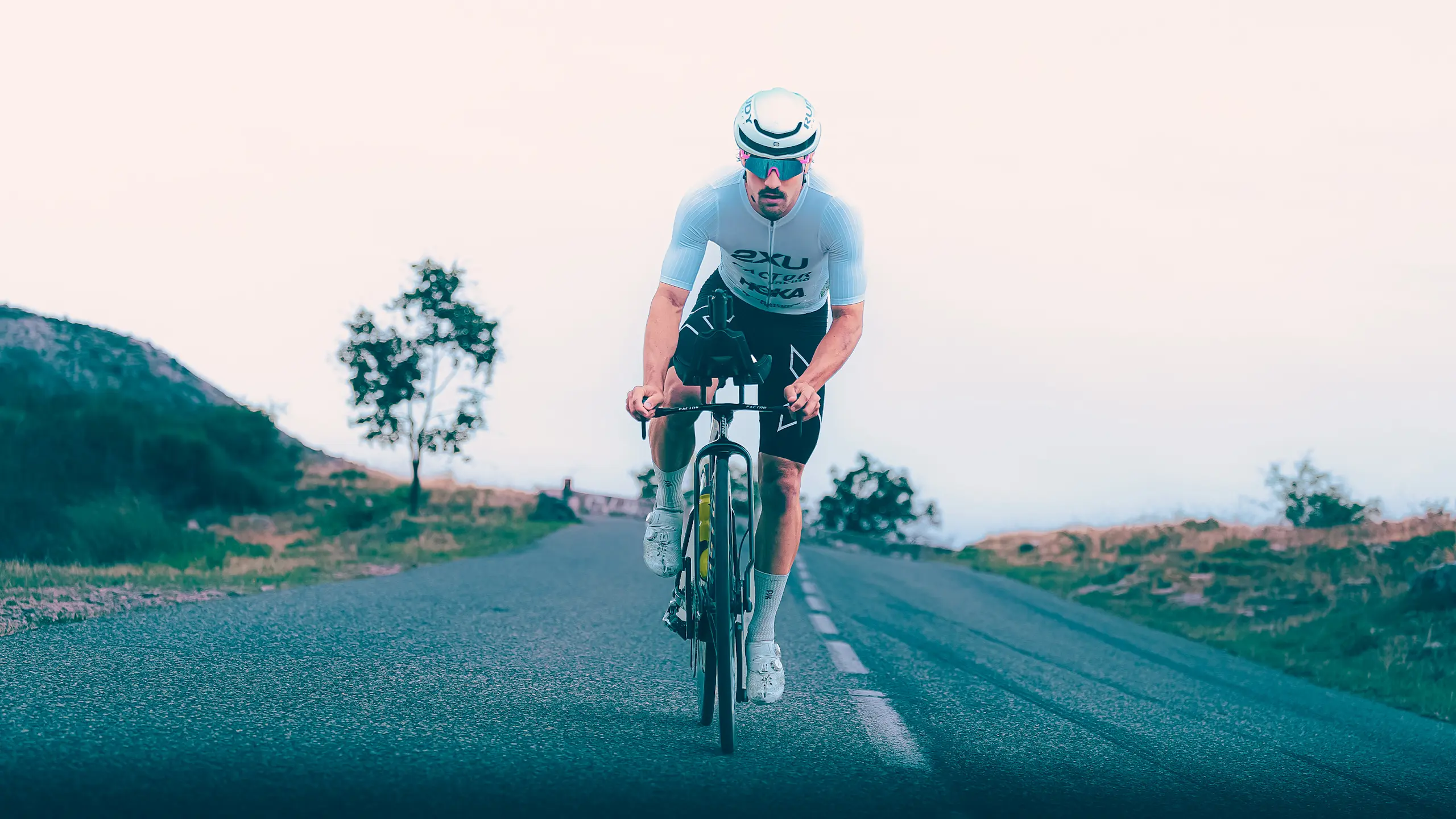 Frontal view of a Factor athlete riding the ONE SP out of the saddle. The wide fork is visible against a cloudy background.