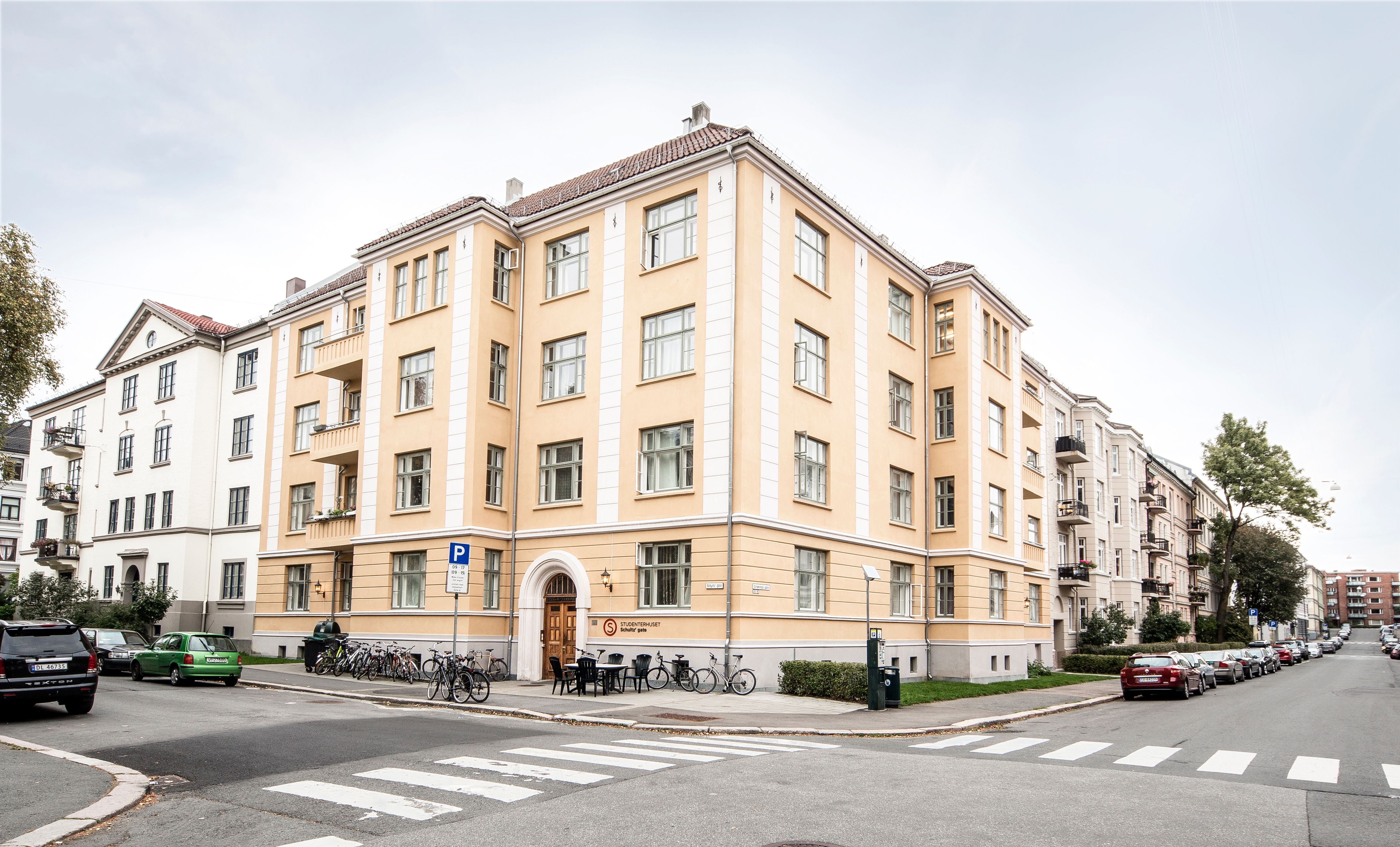 A picture of the corner of the student house in Schultz Gate. The picture shows a yellow building located at a road intersection. There are bicycles parked outside.
