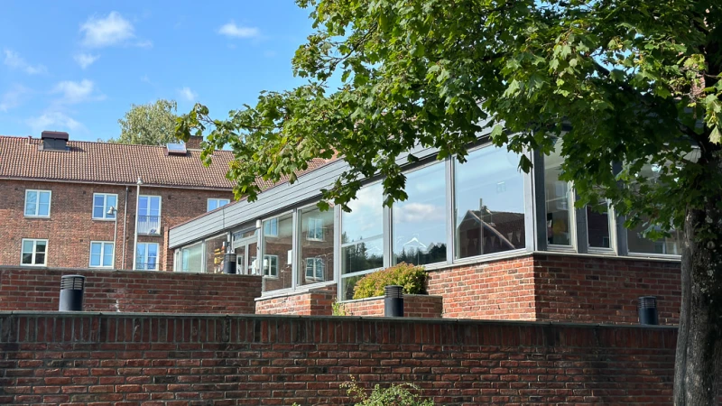 A photo of a brick building with large windows and a green tree in front. 