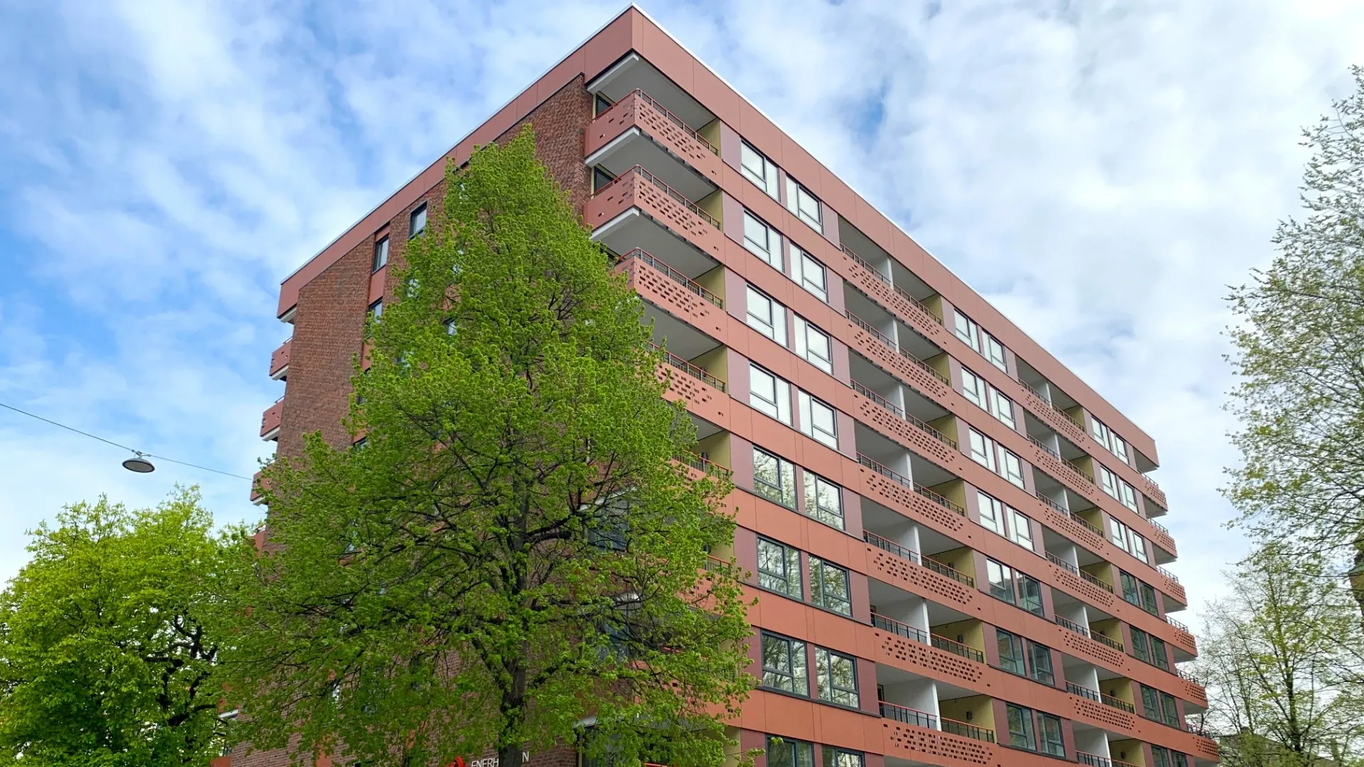 Et bilde av Enerhaugen Studenthus. Bildet viser en rød høyblokk med balkonger. Det er flere trær rundt studenthuset. 