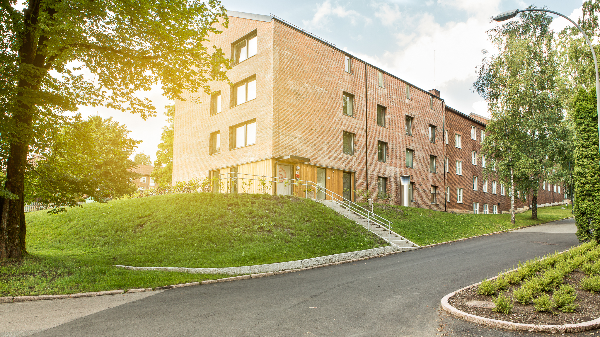 Et bilde av Sogn Studentby. Bildet viser et brunt murbygg som ligger langs en liten vei. Det er en gressplen med trær utenfor bygget. 