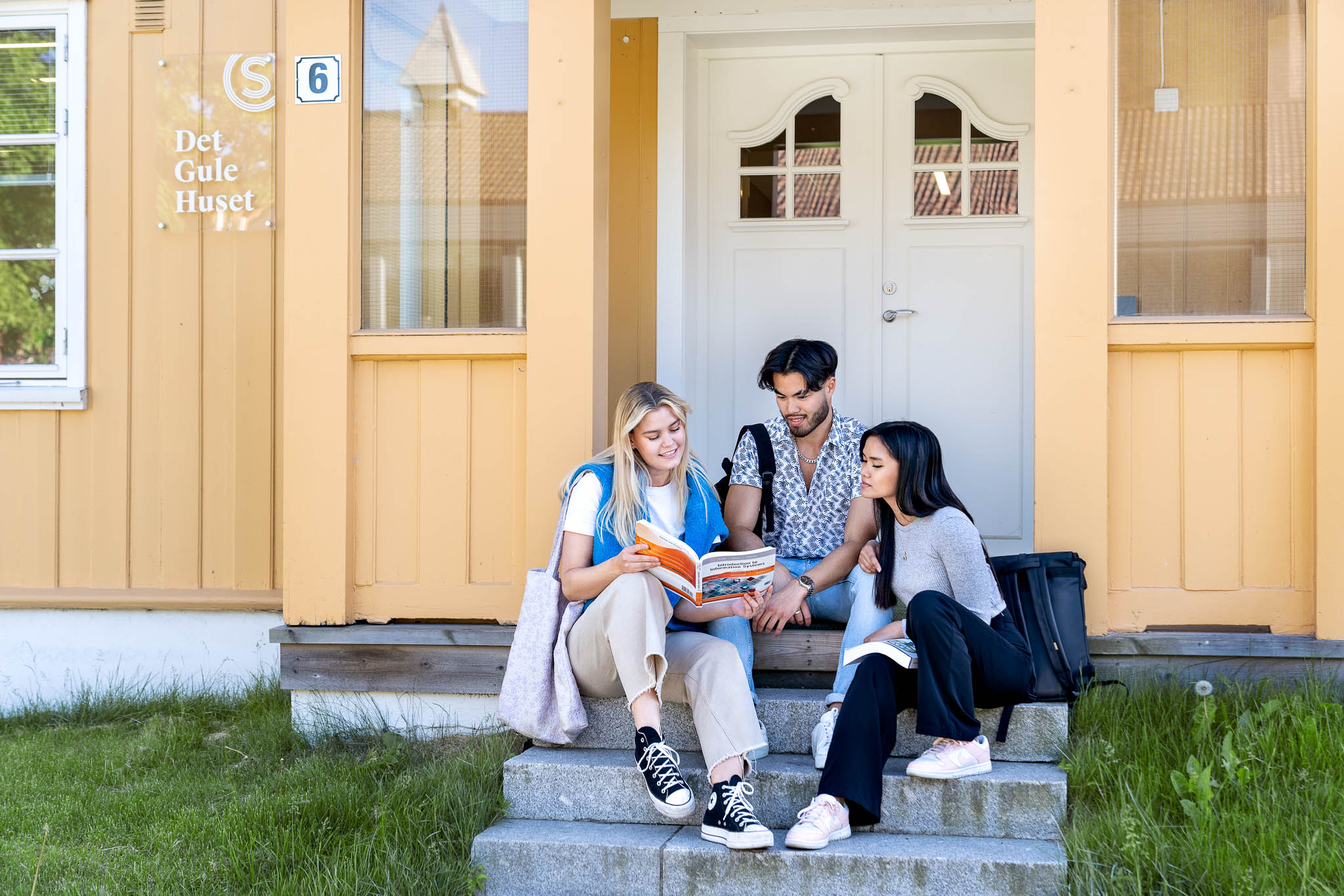Et bilde av det Gule Huset på Sogn. Tre studenter sitter på trappen til inngangen av huset. 