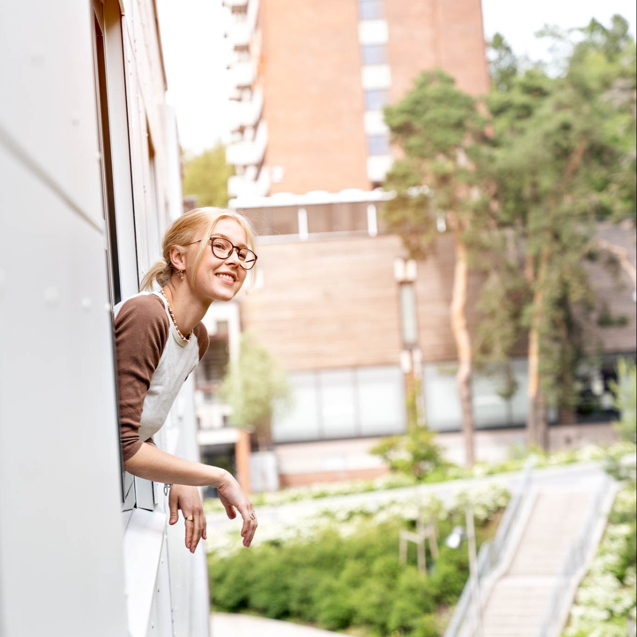 Picture of a student who is leaning out of her window in her apartment in Kringsjå. 