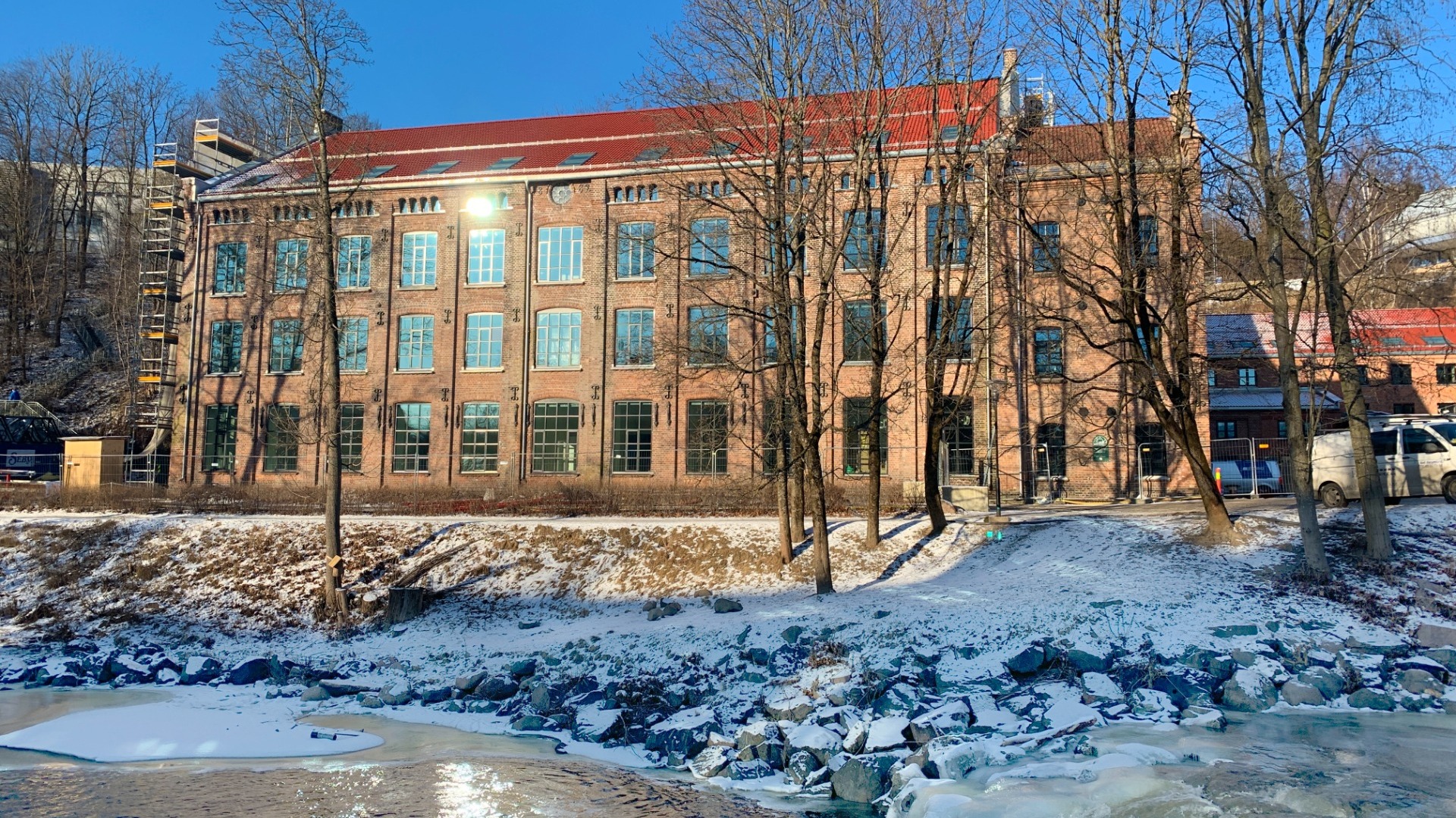 Et bilde av Nydalen Studentby. Bildet viser et rødt murbygg med store vinduer. Bygget ligger ved siden av en elv. 