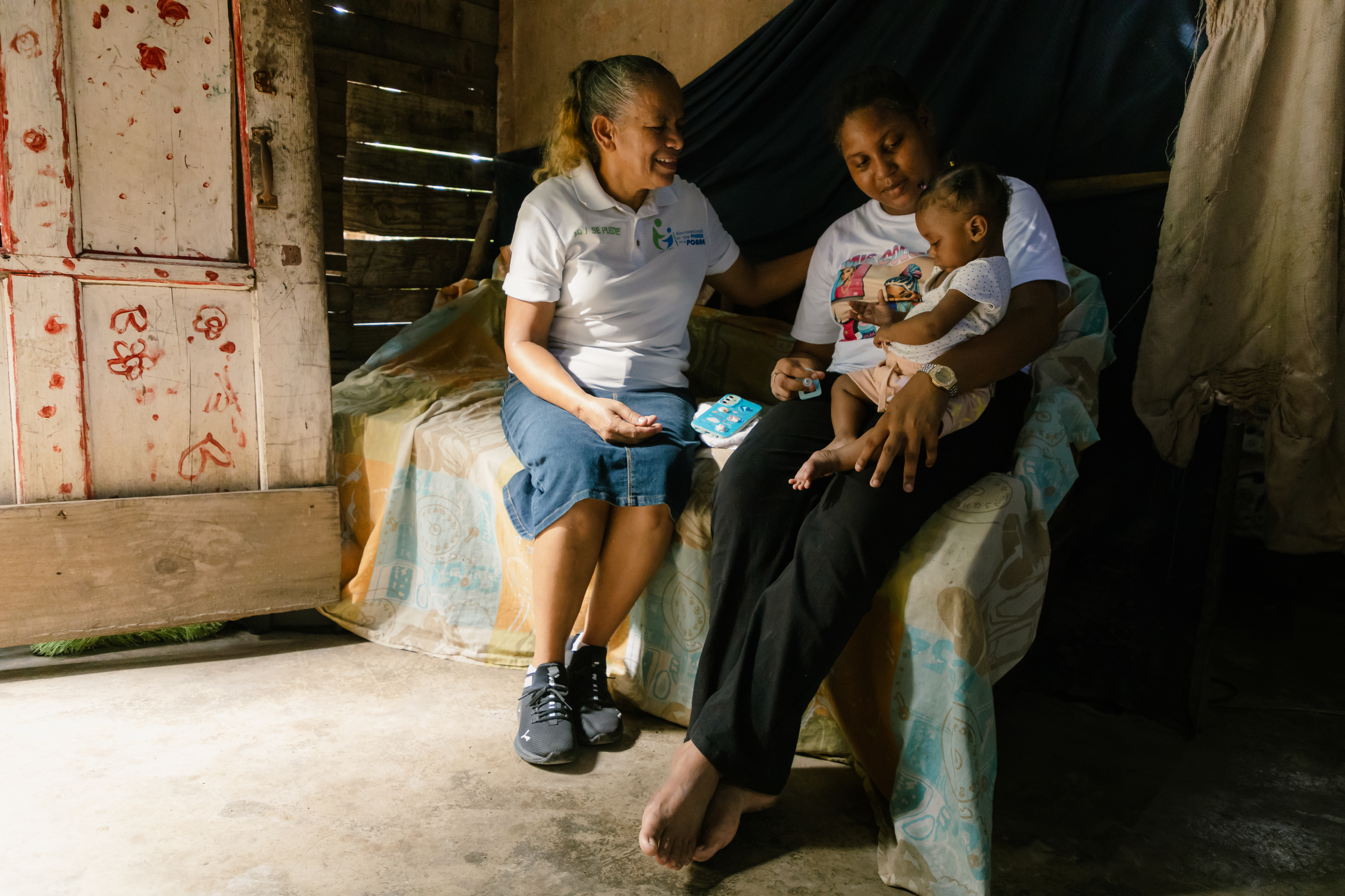 A Survival Implementer sits with a baby and mother to check up on them.