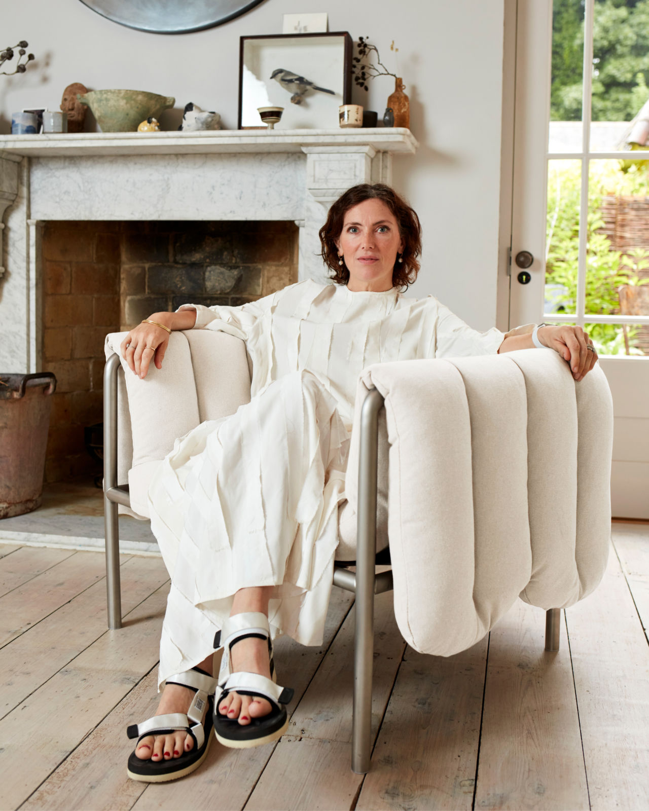 An editorial image of designer Faye Toogood sitting in her own design, the Puffy Lounge Chair in Natural / Stainless.