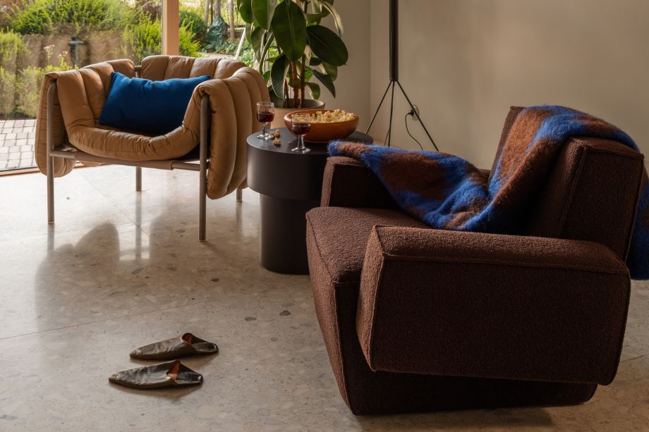 A lifestyle image of a living room scene featuring Puffy Lounge Chair, Storm Cushion Large, Stump Side Table, Hunk Lounge Chair with Armrests, and Monster Throw.