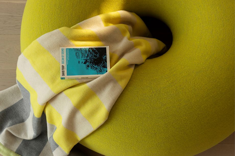 Hem - Boa Pouf in Sulfur Yellow with a Yellow / Gray Stripe Throw placed on top.