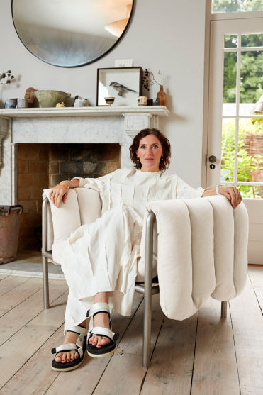 An editorial image of designer Faye Toogood sitting in her own design, Puffy Lounge Chair in Natural / Stainless.