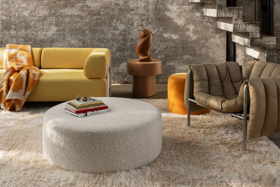 A lifestyle image of a living room/lounge scene featuring Monster Rug, Monster Throw, Bon Pouf Round Large, Bon Pouf, Palo Modular Sofa, Stump Side Table, and Puffy Lounge Chair.