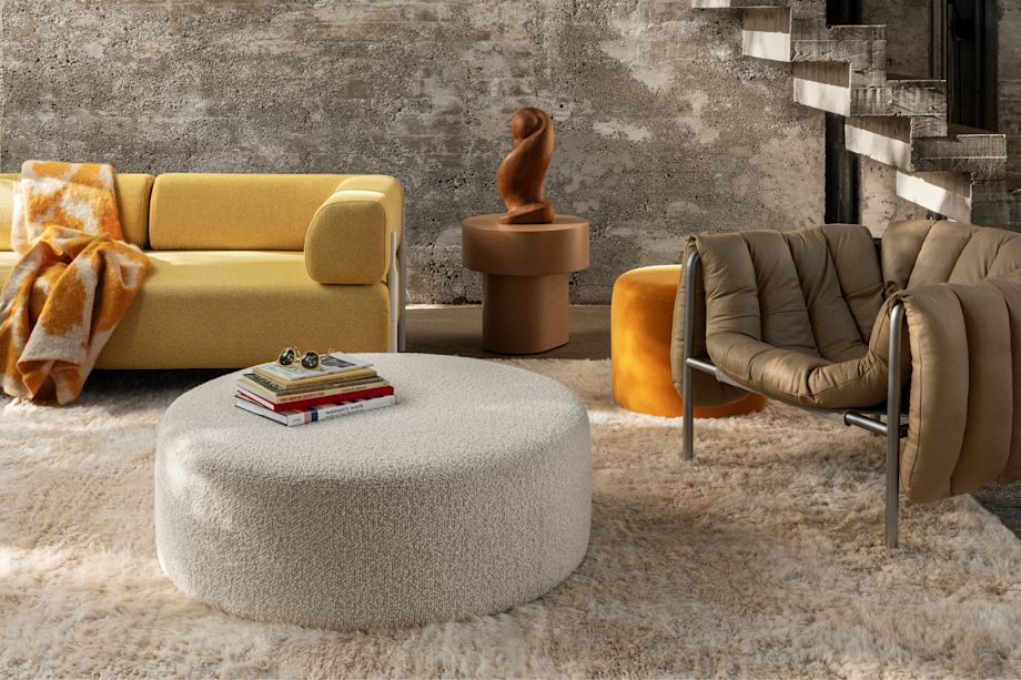A lifestyle image of a living room/lounge scene featuring Monster Rug, Monster Throw, Bon Pouf Round Large, Bon Pouf, Palo Modular Sofa, Stump Side Table, and Puffy Lounge Chair.