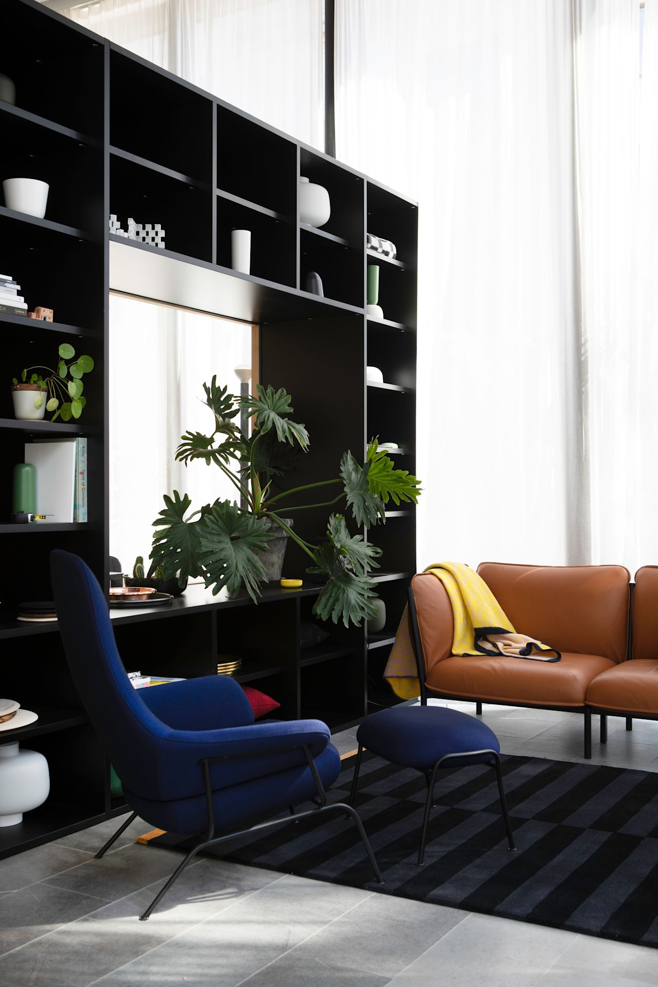 A lifestyle image of a lounge scene from the Hem Headquarters in Stockholm, Sweden in 2018 featuring Kumo Sofa, Hai Lounge Chair + Ottoman, Stripe Rug and Arch Throw.