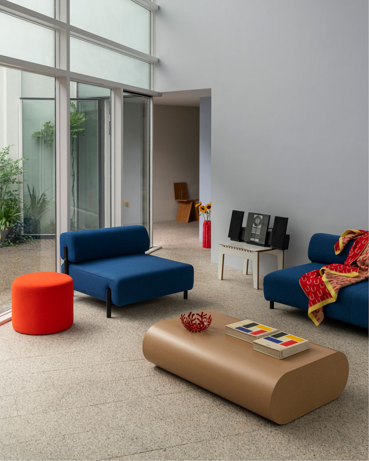 A lifestyle image of a living room scene featuring Palo Modular Single Seater Sofa, Bon Pouf Round, Stump Coffee Table Large, and Arch Throw.