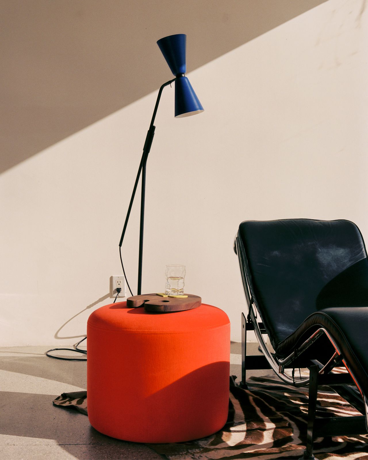 A lifestyle image of a lounge scene featuring Bon Pouf Round Red, Alphabeta Floor Lamp, and Palette Cutting Board Small.