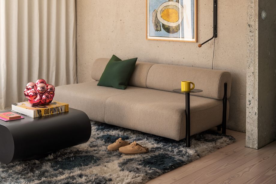 A lifestyle image of a living room scene featuring Palo Modular Sofa, Neo Cushion Medium, Palo Side Table, Monster Rug, Stump Coffee Table, Bronto Tableware, and Moln, a Hem X limited edition piece.