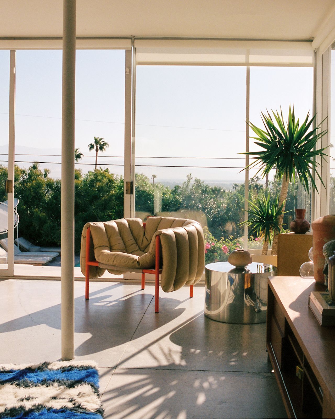 A lifestyle image of a lounge scene featuring Puffy Lounge Chair Sand Leather / Traffic Red and Monster Rug Ultramarine Blue / Off-white.