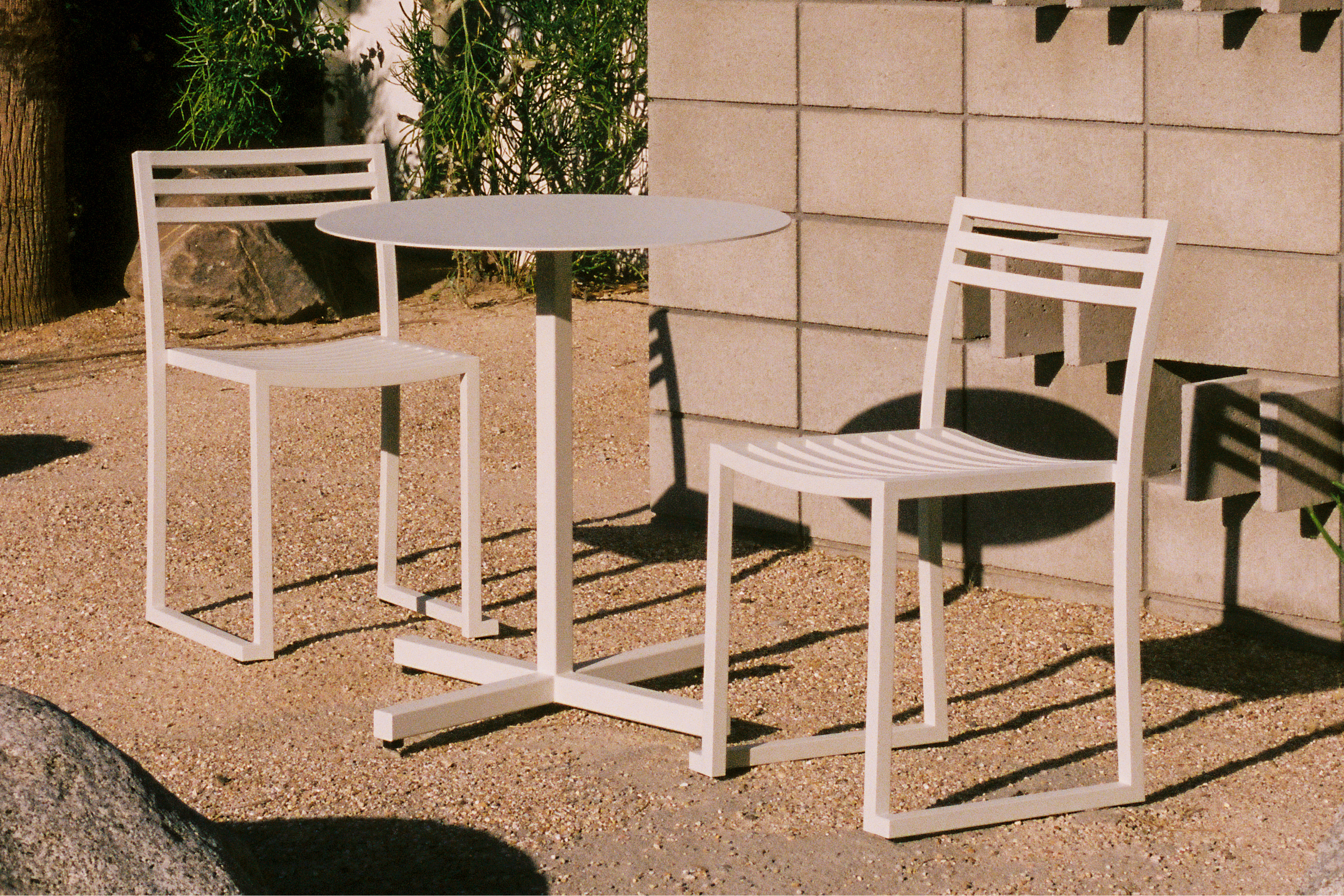 A lifestyle image of an outdoor patio scene featuring Chop Table Round Grey White and Chop Chair (Set of 2) Grey White.