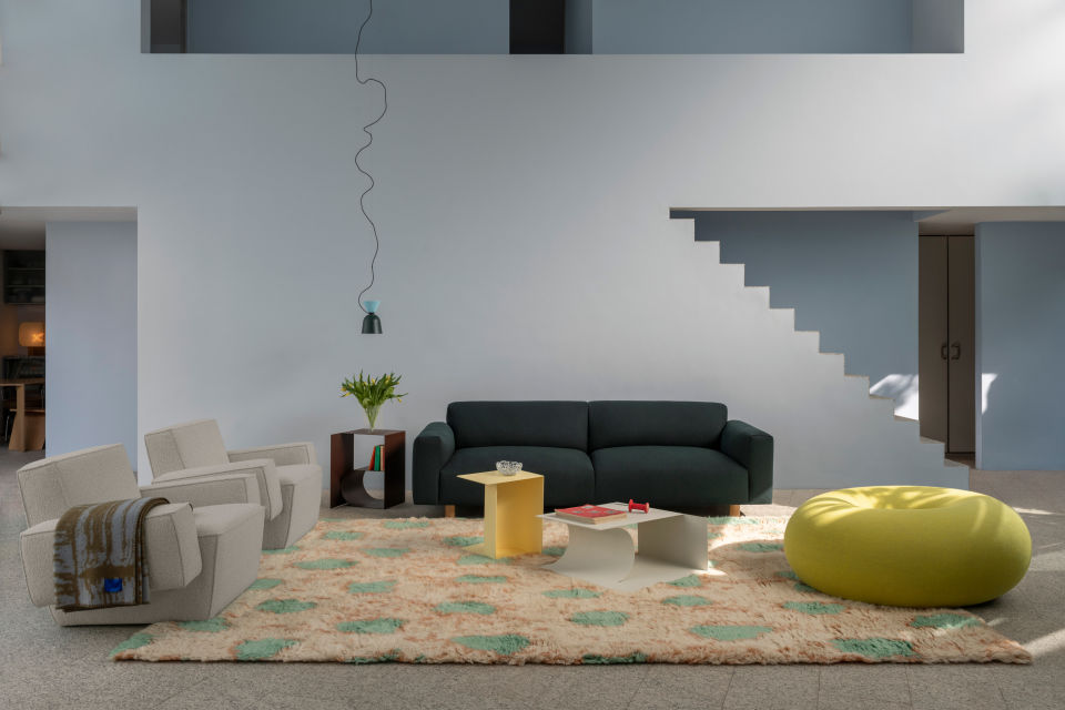 A lifestyle image of a living room scene featuring Hunk Lounge Chairs with Armrests, Alphabeta Pendant Light, Glitch Throw, Koti 3-seater Sofa, Monster Rug, Glyph Side Tables, and Boa Pouf.