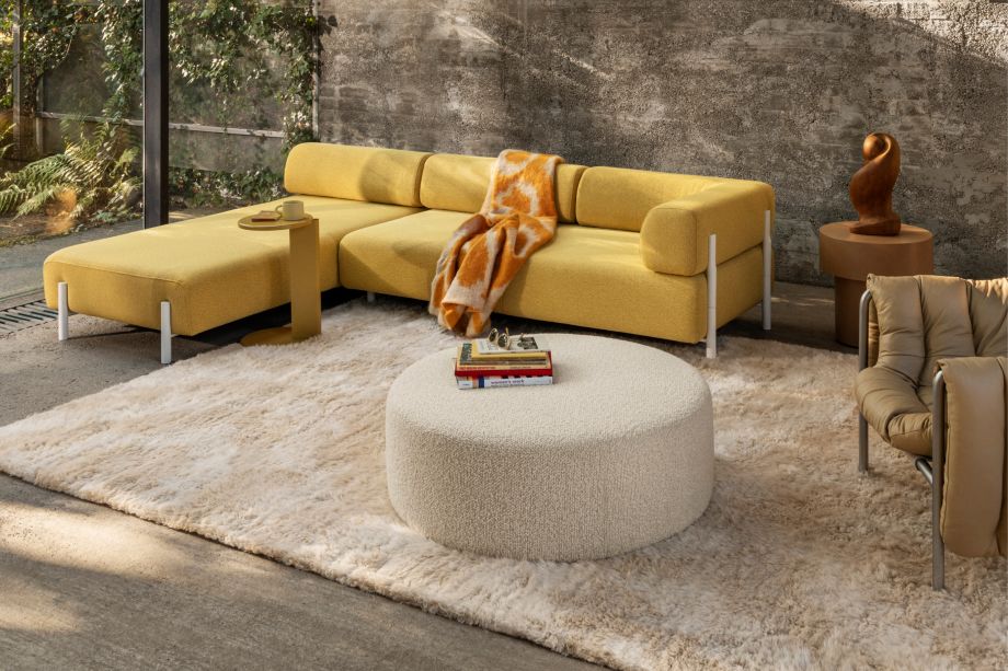 Hem - A living room scene featuring Palo Modular Corner Soft Left Sunflower, Lolly Side Table Ochre Yellow, Monster Throw Ochre / Off-White Ring, Monster Rug Beige / Off-White, Bon Pouf Round Large Eggshell, Stump Side Table Natural, and a Puffy Lounge Chair.