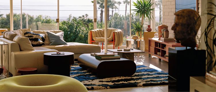 A lifestyle image of a living room/lounge scene featuring Monster Rug Ultramarine Blue/Off-white, Boa Pouf, Puffy Lounge Chair, Stump Side Table, Stump Coffee Table Large, Velvet Cushion Medium, and Monster Cushion Medium.