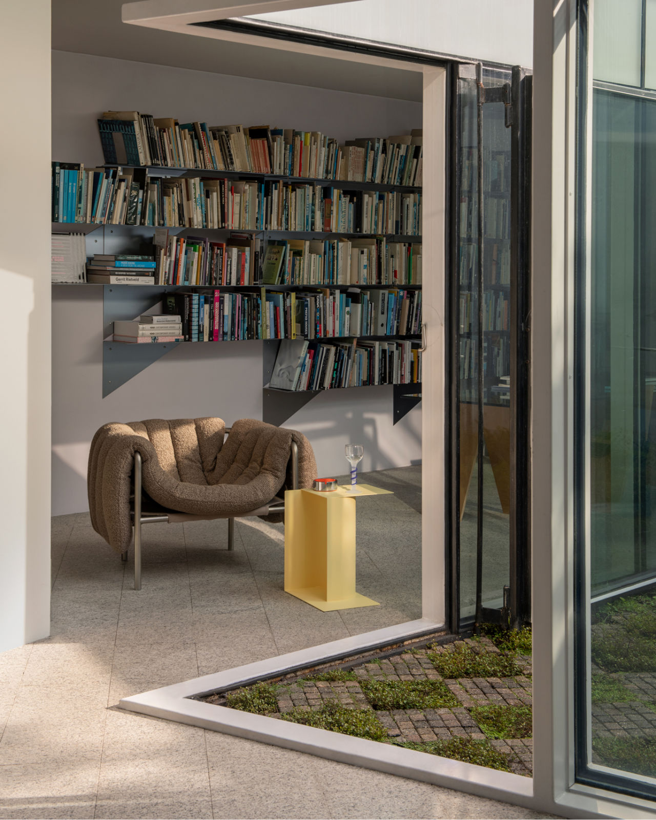 A lifestyle image of a lounge scene featuring Puffy Lounge Chair Sawdust / Stainless and Glyph Side Table Gamma Wax Yellow.