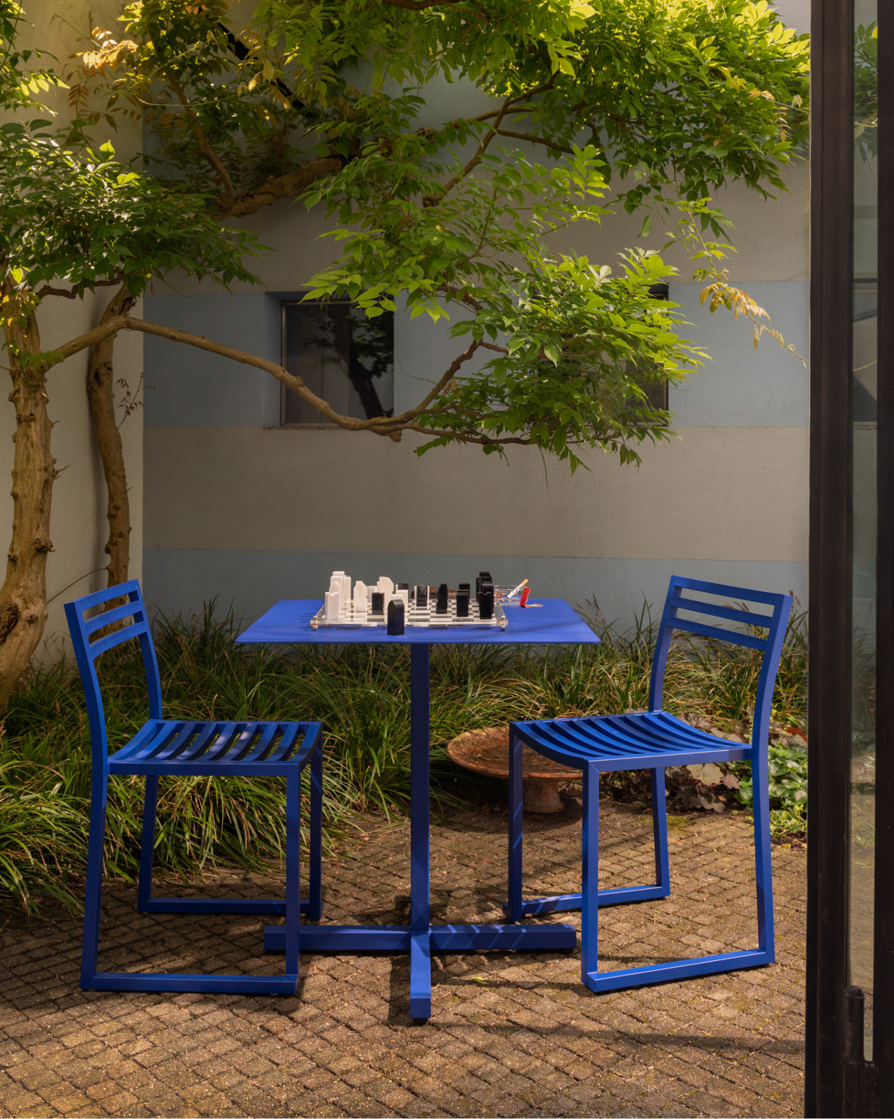 A lifestyle image of an outdoor scene featuring Chop Chairs and Chop Table Square in Ultramarine Blue.