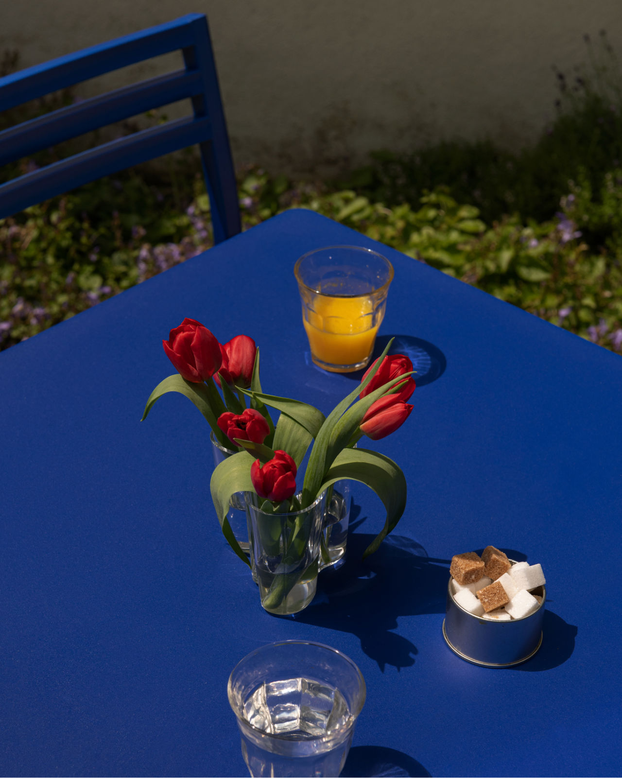 A lifestyle image of an outdoor scene featuring Chop Table Square and Chop Chair in Ultramarine Blue.