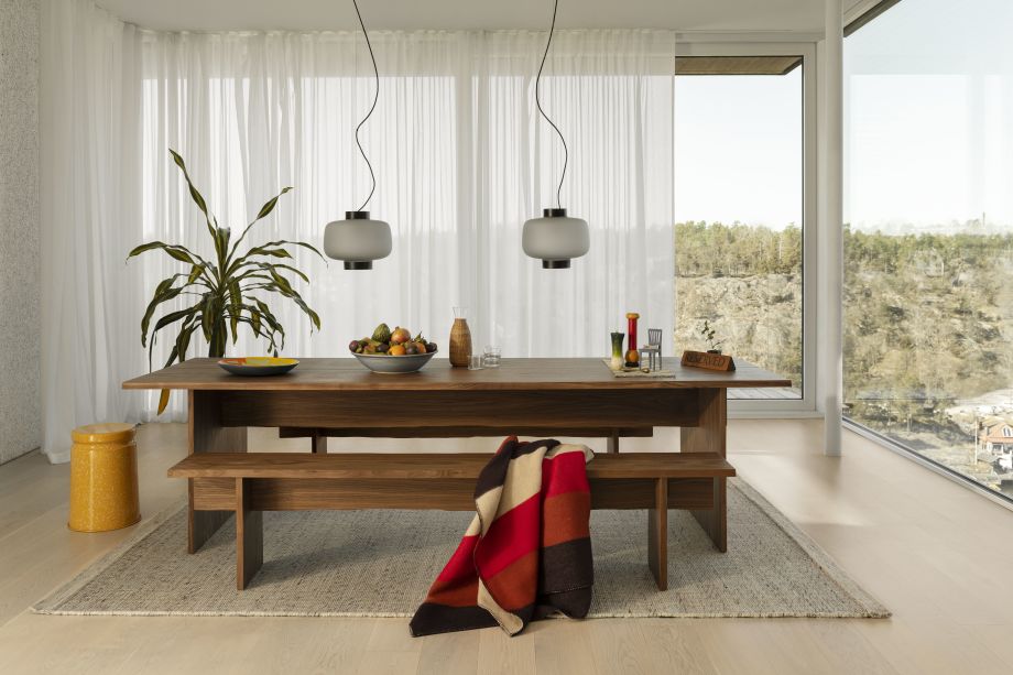 A lifestyle image of a dining scene featuring Bookmatch Table + Benches Set in Walnut, Dusk Lamp, Last Stool, Block Throw, Offcut Plate and Dune Rug Large.