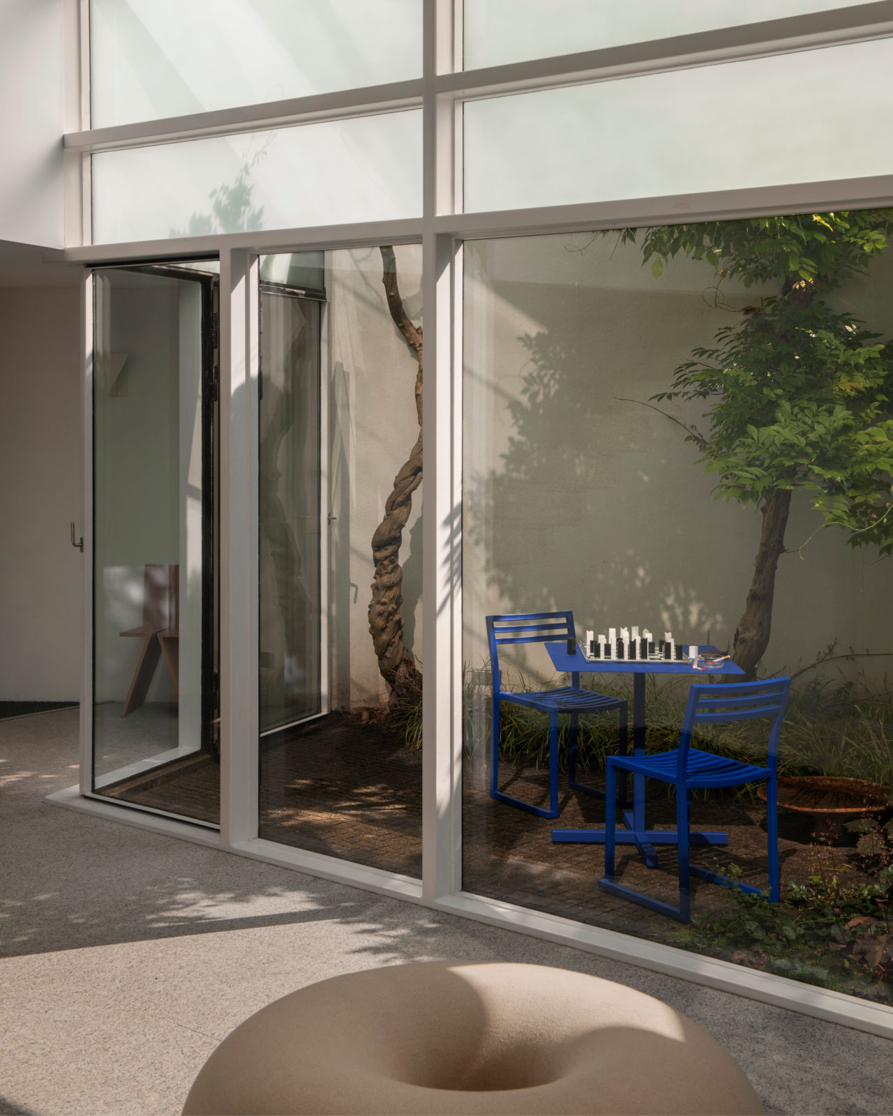 A lifestyle image of an indoor/outdoor scene featuring Chop Chair and Chop Table Square in Ultramarine Blue and Boa Pouf in Oatmeal.