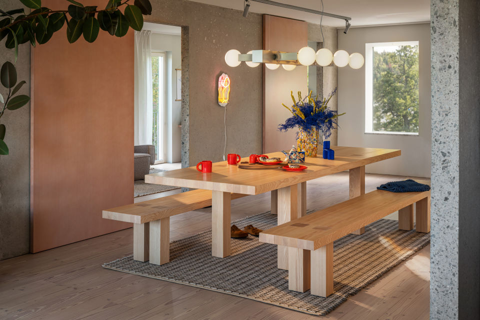 A lifestyle image of a dining scene featuring Knuckle Linear Chandelier, Bronto Tableware, Max Table + Benches Set, Rope Rug, Brute Vase, and Globos Neon.
