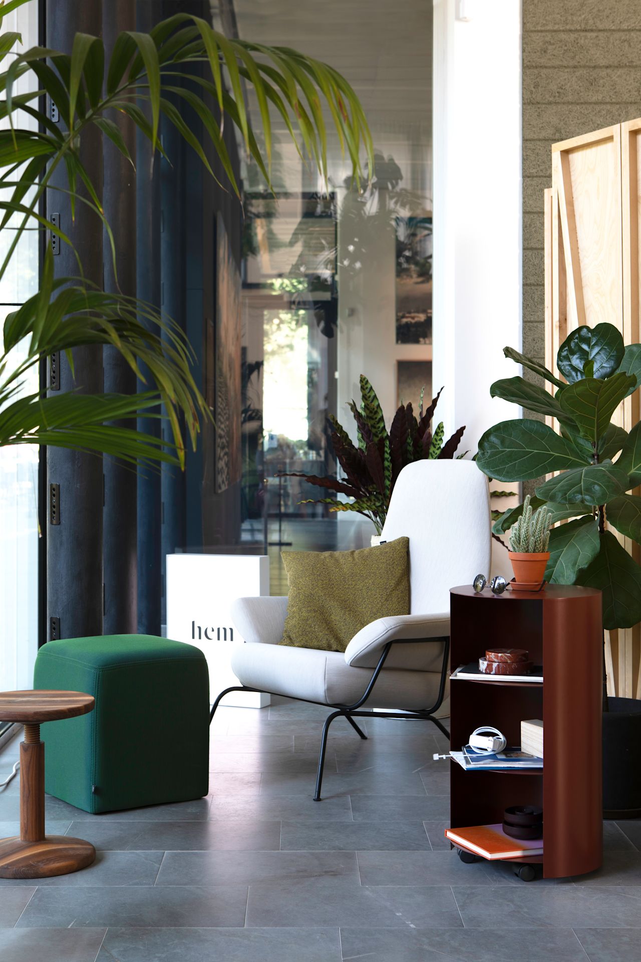 A lifestyle image of a lounge scene from the Hem Headquarters in Stockholm, Sweden in 2018 featuring Hai Lounge Chair, Bon Pouf Cube, All Wood Stool, Hide Pedestal and Melange Cushion.