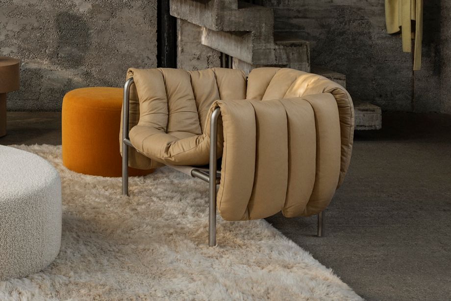 Hem - A living room scene featuring a Puffy Lounge Chair in Sand Soft Leather / Stainless Steel on top of a Monster Rug in Beige / Off-White. In the background is a Bon Pouf Round in Ochre and a Bon Pouf Round Large in Eggshell.