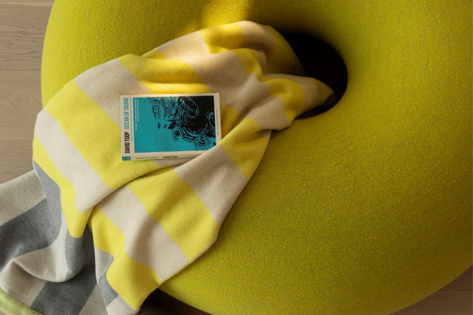 Hem - Boa Pouf in Sulfur Yellow with a Yellow / Gray Stripe Throw placed on top. 