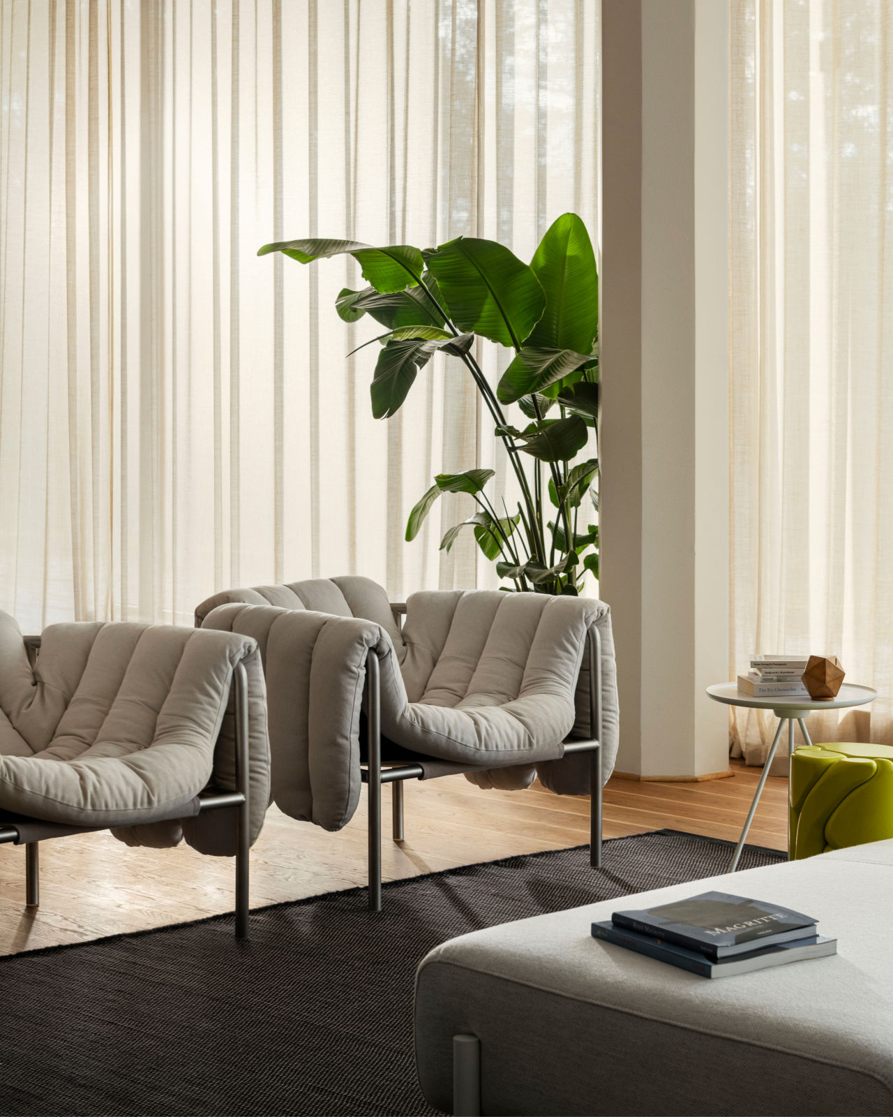 A lifestyle image of a lounge scene featuring Puffy Lounge Chair, Dune Rug, Palo Modular Sofa, and Key Side Table.