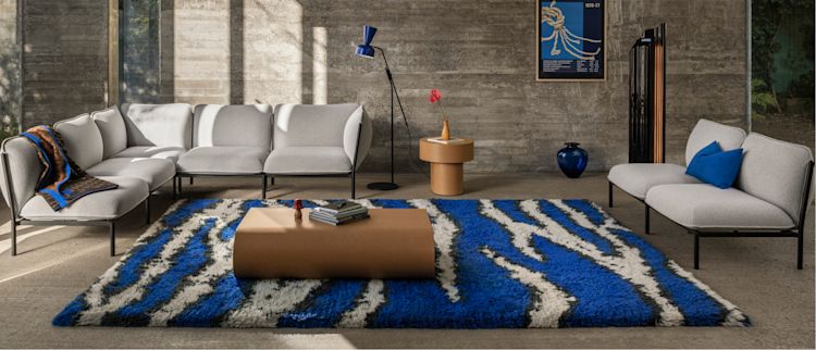 Hem - A living room scene featuring Kumo Sofas in Porcelain, Monster Rug Ultramarine Blue / Off-White, Arch Throw Black / Brown / Blue, Stump Coffee Table Medium Natural, Alphabeta Floor Lamp Blue, Stump Side Table Natural, and Storm Cushion Large Sky.