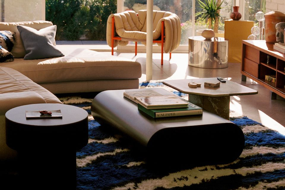 A lifestyle image of a living room scene featuring Monster Rug Extra Large, Stump Side Table, Stump Coffee Table Large, Velvet Cushion Medium, and Puffy Lounge Chair.