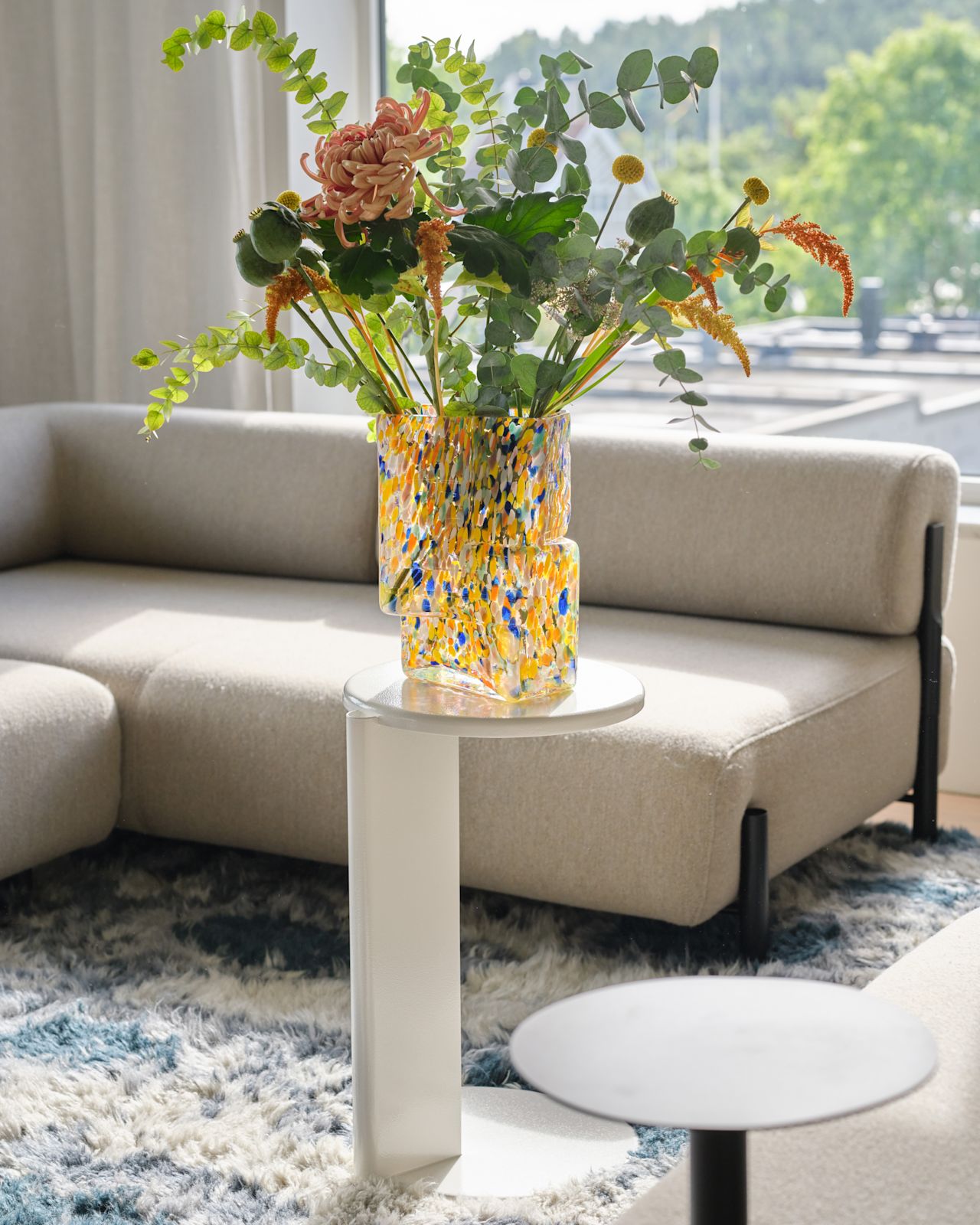 A lifestyle image of a living room scene featuring Palo Modular Sofa and Side Table, Lolly Side Table, Brute Vase, and Monster Rug.