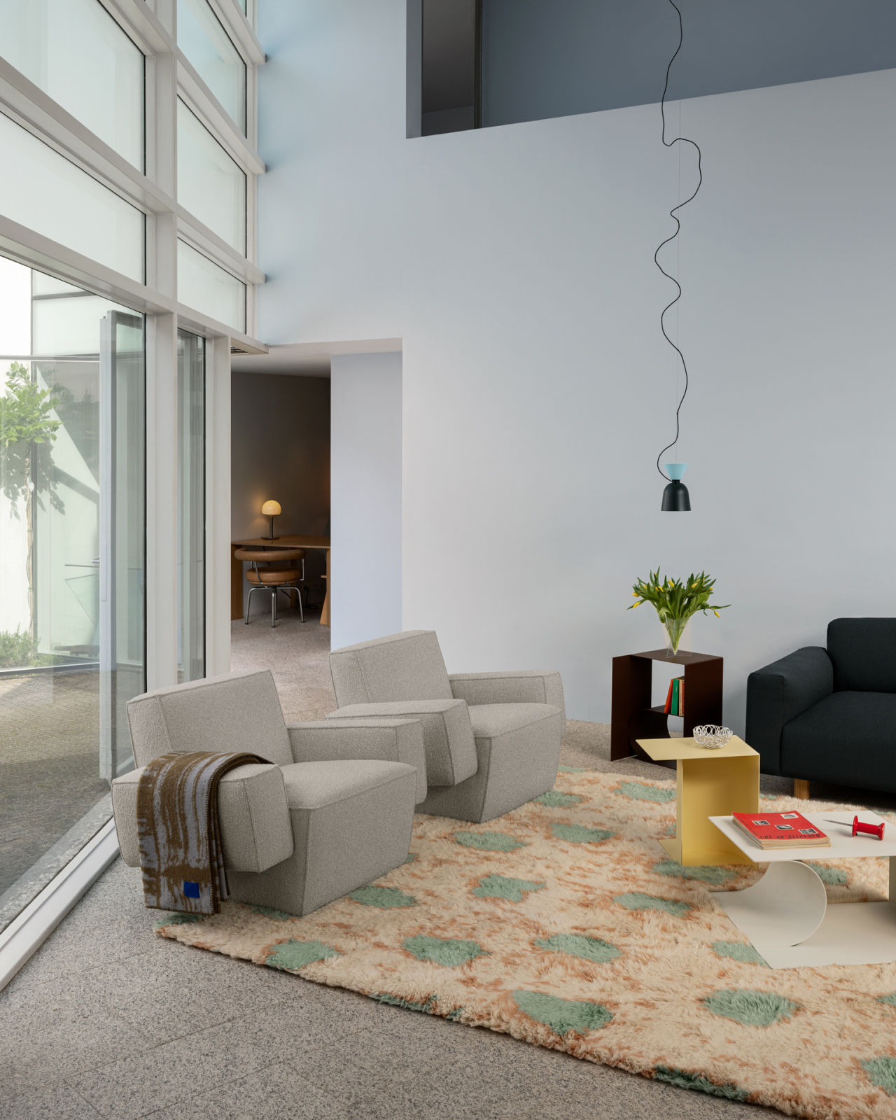 A lifestyle image of a living room scene featuring Hunk Lounge Chair with Armrests, Glitch Throw, Monster Rug, Alphabeta Pendant Light, Glyph Side Tables, and Koti Sofa.