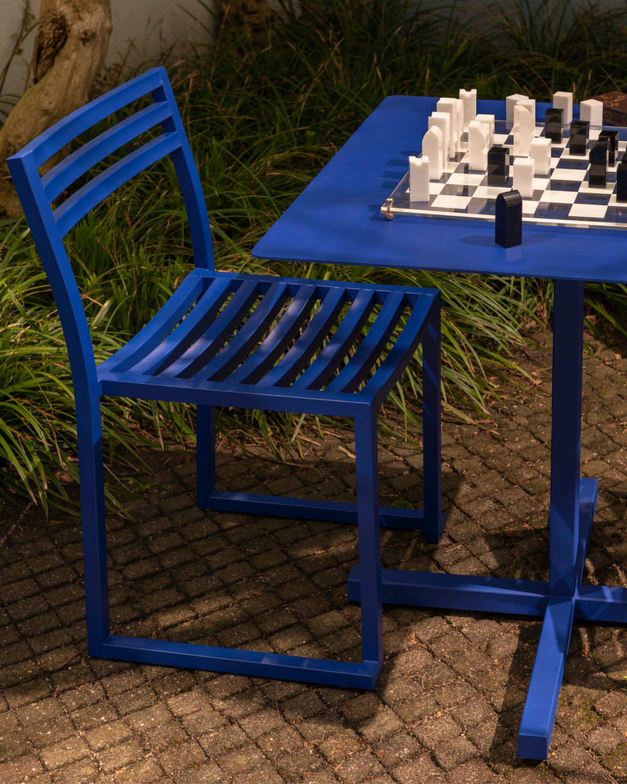 A lifestyle image of an outdoor scene featuring Chop Chair and Chop Table Square in Ultramarine Blue.