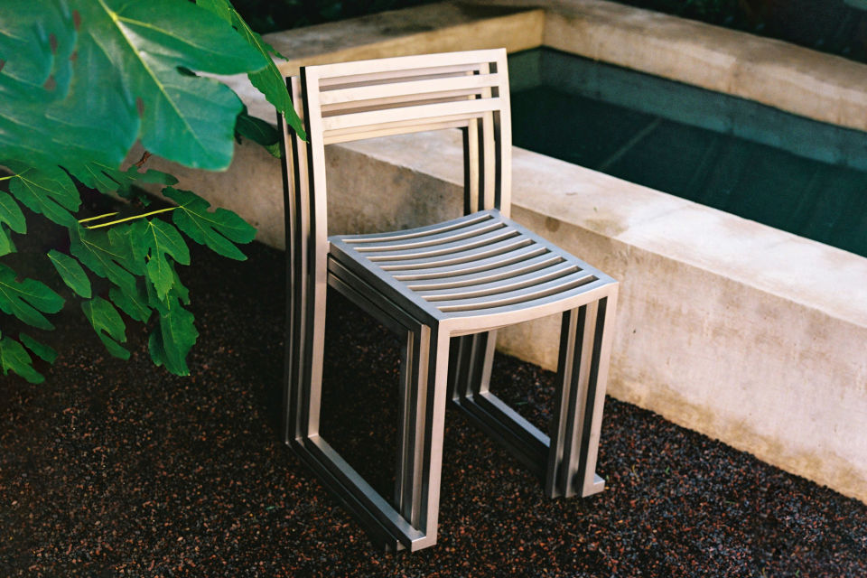 A lifestyle image of an outdoor scene featuring Chop Chairs in Stainless stacked together.