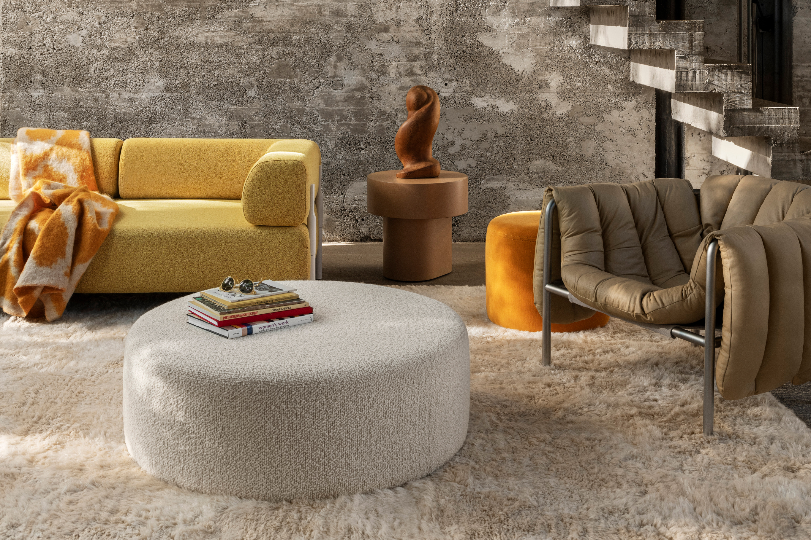 A lifestyle image of a living room/lounge scene featuring Monster Throw, Monster Rug, Palo Modular Sofa, Stump Side Table, Bon Pouf Round Large, Bon Pouf, and Puffy Lounge Chair.